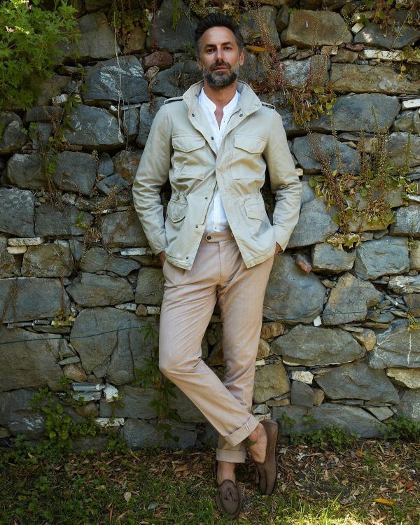 Foto toont moderne man met een zomerjack in kleur beige staand tegen een muur
